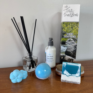 Pacific Northwest Scented Collection of soap, bath bomb, shower steamers, body lotion and reed diffuser on a wooden counter