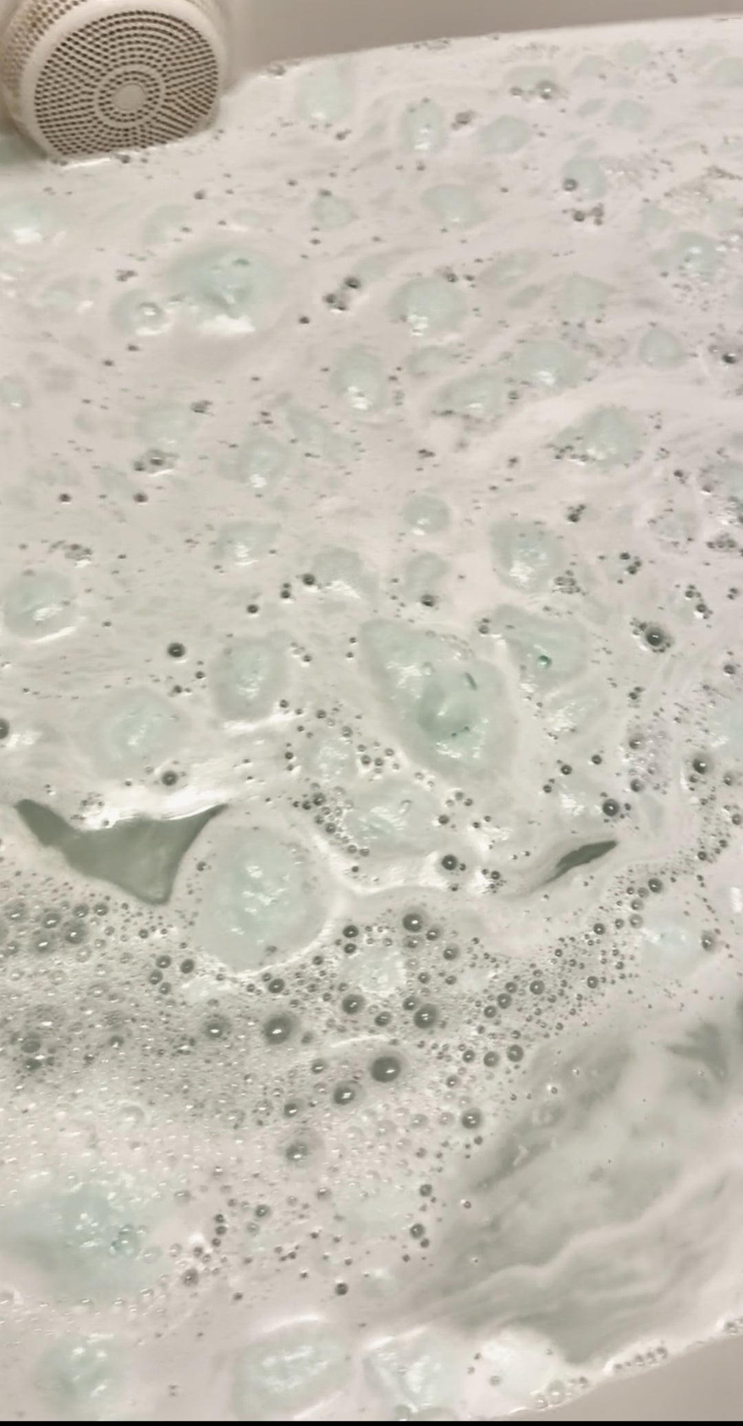 A bath crumble dissolving in a bubble bath, releasing a creamy white liquid with a vanilla scent.