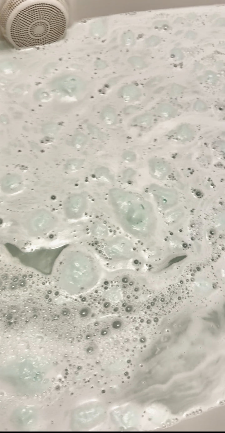 A bath crumble dissolving in a bubble bath, releasing a creamy white liquid with a vanilla scent.