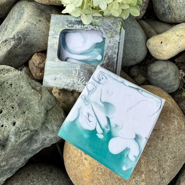 Blue Driftwood Soap Aloe Vera, Olive Oil and Shea Butter sitting on rocks.  Scented with Sandalwood in soft purple and blue colors