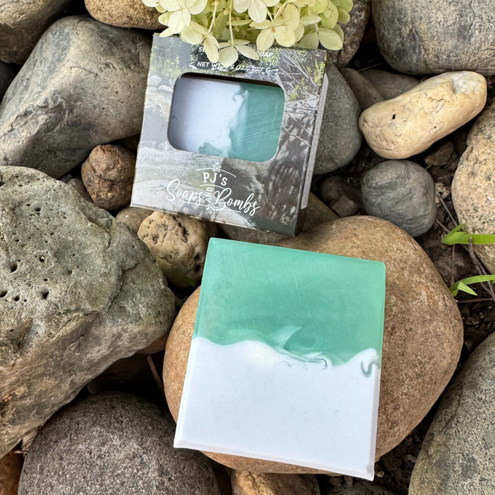 Serentity Grove Aloe Vera, Olive Oil and Shea Butter Soap.  Palo Santo Scent in Soft Green and Blue colors sitting on rocks 