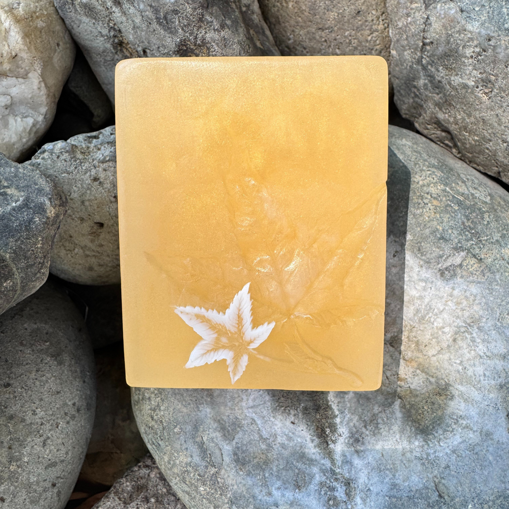 Yellow rectangular soap with a small white leaf design on a bed of rocks